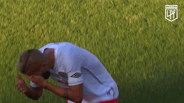 a man in a white shirt and red shorts is kneeling down on a grassy field with a nfl logo in the background