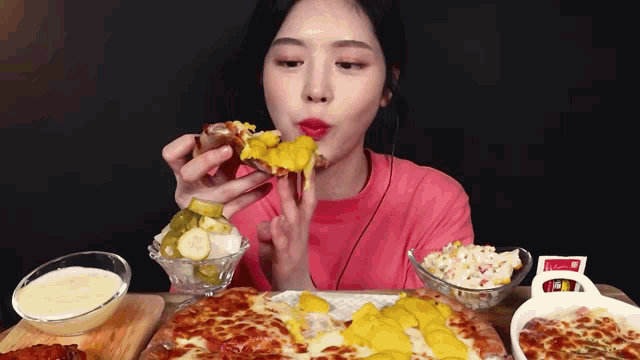a woman in a pink shirt is eating a pizza with pickles and cheese