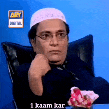 a man wearing glasses and a white hat is sitting in front of a ary digital sign