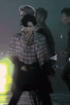 a man in a plaid jacket is dancing in front of a green light