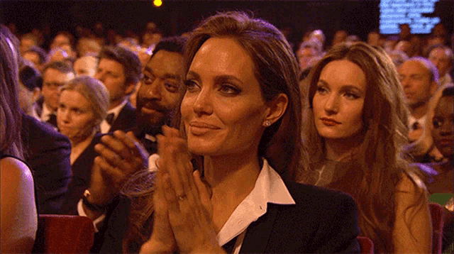 a woman in a black suit applauds in a crowd