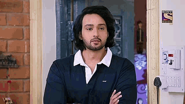 a man with a beard and long hair is standing in a doorway with his arms crossed .