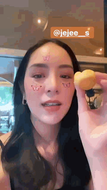 a woman with a butterfly on her face is holding a heart shaped cookie