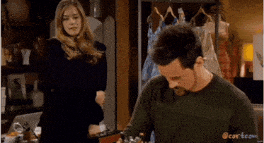 a man and a woman are standing next to each other in a room with clothes hanging on a rack