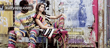 a man and a woman are sitting next to each other in front of a wall with graffiti on it .