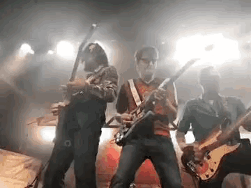 three men are playing guitars on a stage in a dark room .