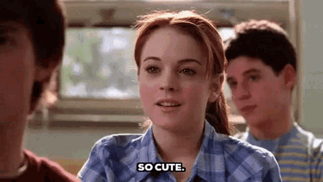 a girl in a plaid shirt is sitting at a table with two boys and says `` so cute '' .