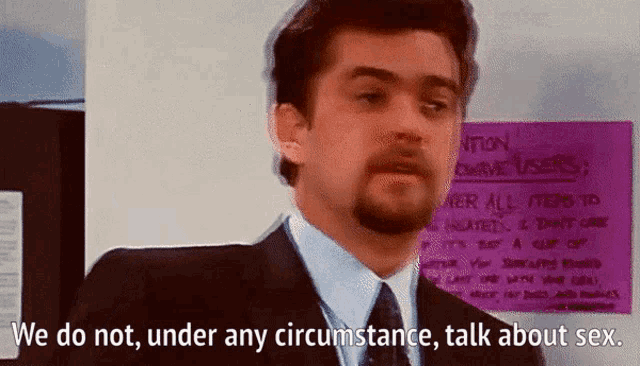 a man in a suit and tie is standing in front of a sign that says we do not under any circumstance talk about sex