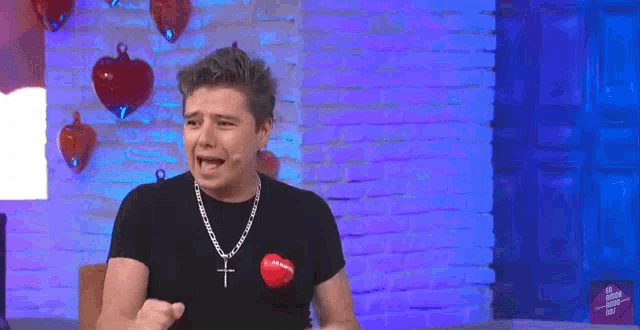 a man wearing a black shirt with a red heart on it and a cross around his neck