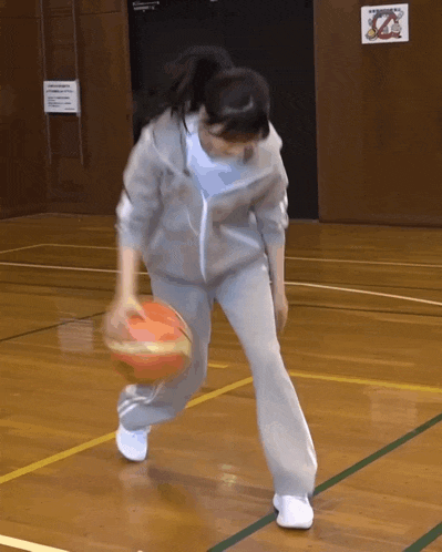 a woman is dribbling a basketball on a court with a sign on the wall that says no smoking