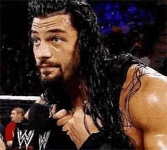 a man with long hair and a beard is standing in a wrestling ring holding a microphone .