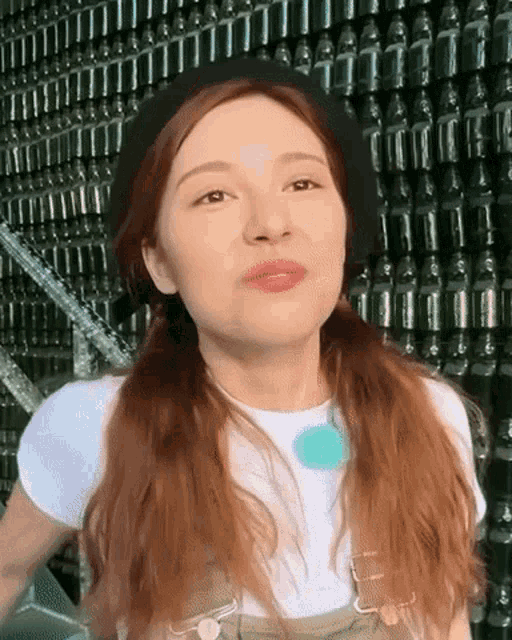 a woman wearing a beret and overalls stands in front of a wall of bottles