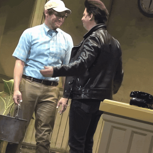a man in a baseball cap talks to a man in a leather jacket