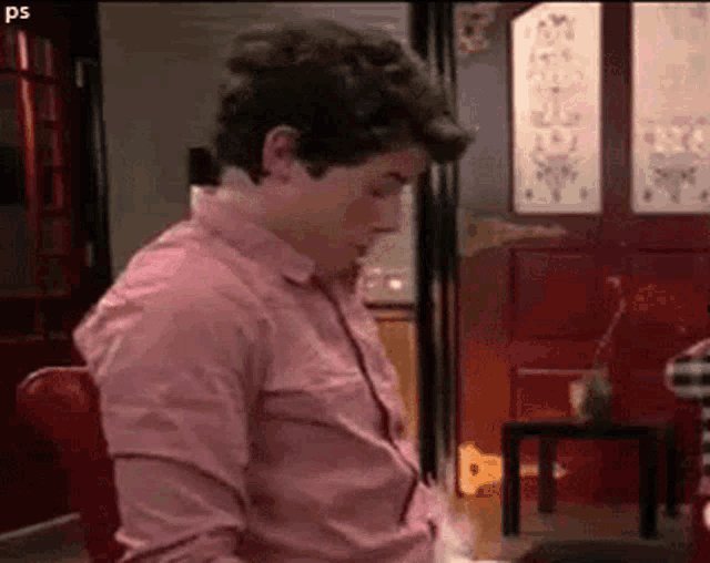 a man in a pink shirt is sitting in a chair in front of a door .