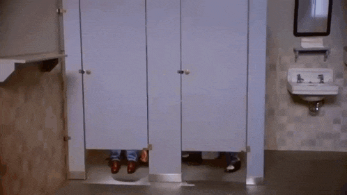 a man is standing in a public restroom behind a stall .