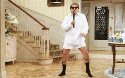 a man in a white shirt and socks is dancing in a living room while holding a microphone .