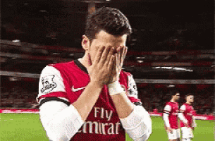 a soccer player wearing a fly emirates jersey covering his face with his hands