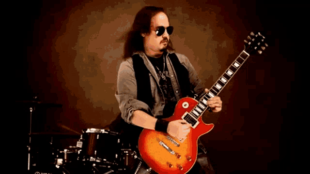 a man wearing sunglasses is playing a guitar in front of a yamaha drum set