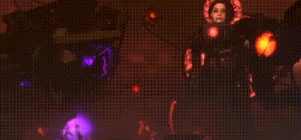a person is standing in front of a fire in a dark room with purple and yellow lights .