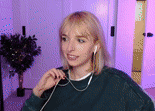 a woman wearing headphones and a green sweater is standing in a room .