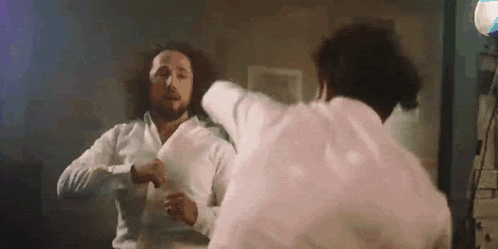 two men are fighting in front of a mirror in a room .