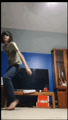 a young boy is dancing in front of a flat screen tv in a living room
