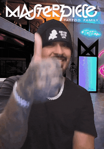 a man giving a thumbs up in front of the masterpiece tattoo family logo