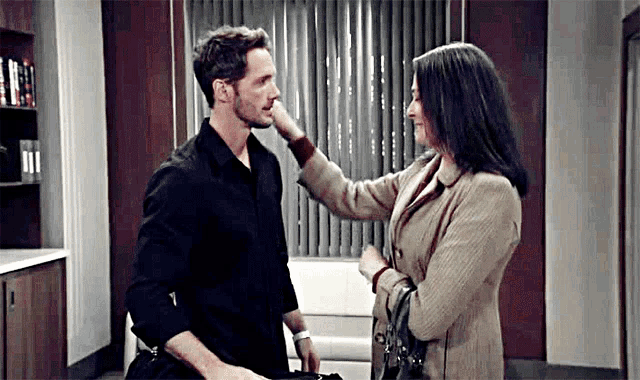 a man and a woman are standing next to each other in a room . the woman is touching the man 's face .