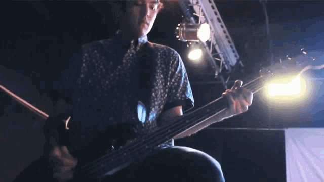 a man playing a guitar in a dark room with the letter h visible in the background