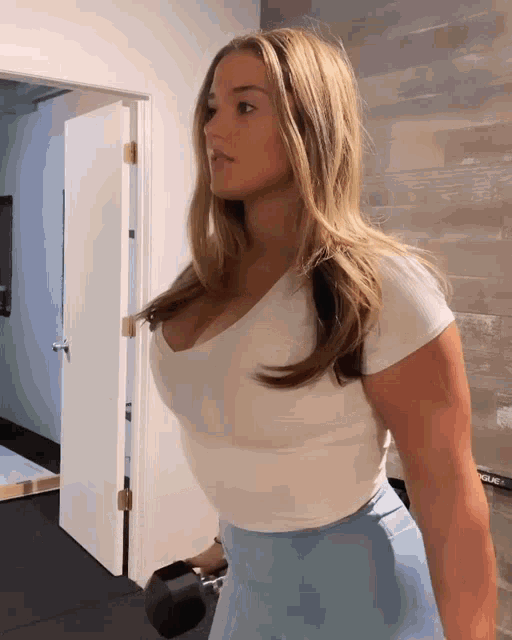 a woman in a white top and blue shorts is holding a dumbbell