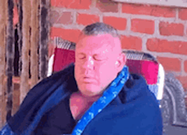a man wrapped in a blue blanket is sitting in a chair with his eyes closed