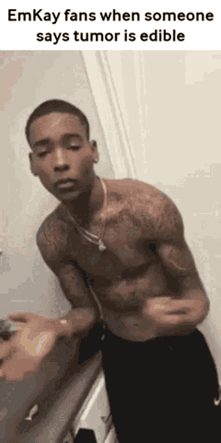 a shirtless man is standing in front of a wall and talking to someone .