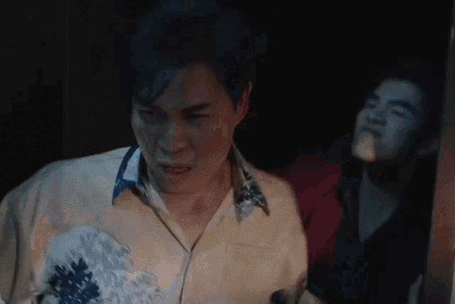 a man is making a funny face in a dark room while another man watches .