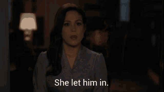 a woman standing in a dark room with the words she let him in behind her
