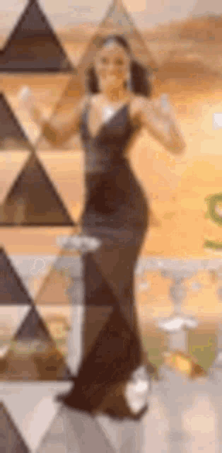 a woman in a black dress is dancing in front of a wall with triangles on it .