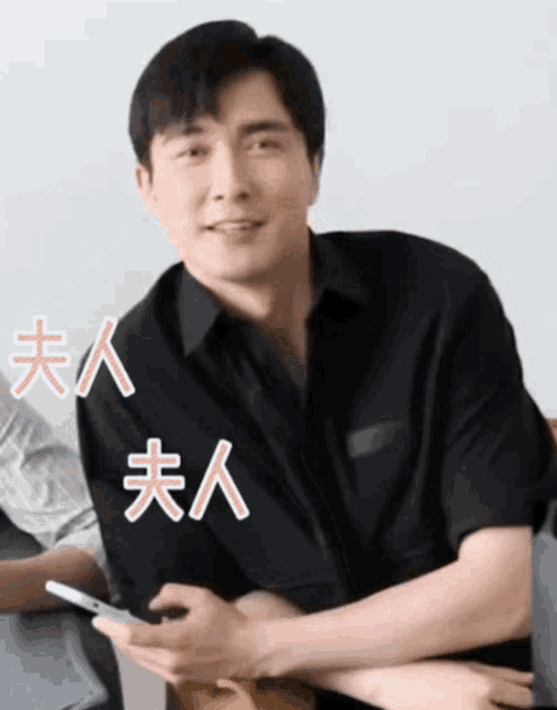 a man wearing a black shirt is holding a cell phone with chinese writing on it