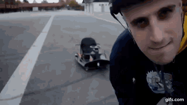 a man wearing a helmet is standing next to a toy car on a street .