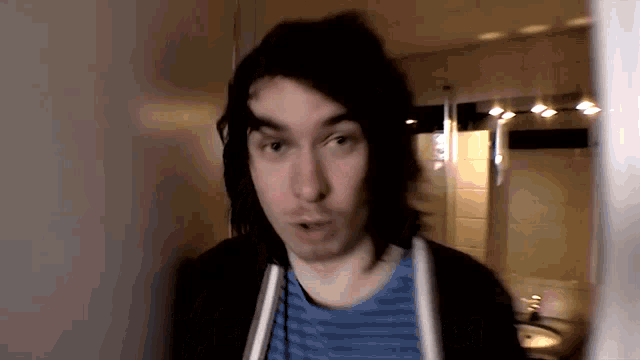 a man with long black hair is standing in front of a bathroom mirror .