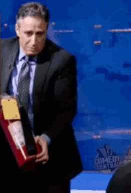 a man in a suit and tie is holding a box in front of a comedy central sign