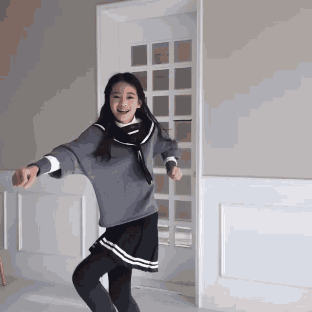 a young girl wearing a sweater and skirt is dancing in front of a door