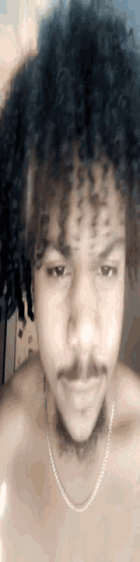 a man with curly hair and a beard is wearing a chain around his neck and looking at the camera .
