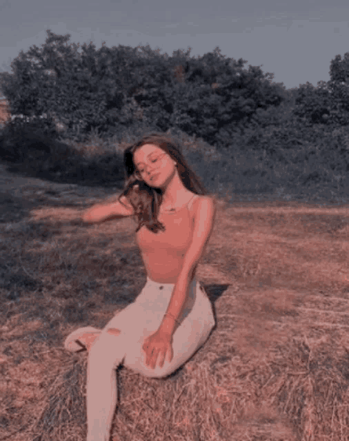 a woman is sitting on a pile of hay in a field