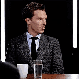 a man in a suit and tie is sitting at a table with a glass of water