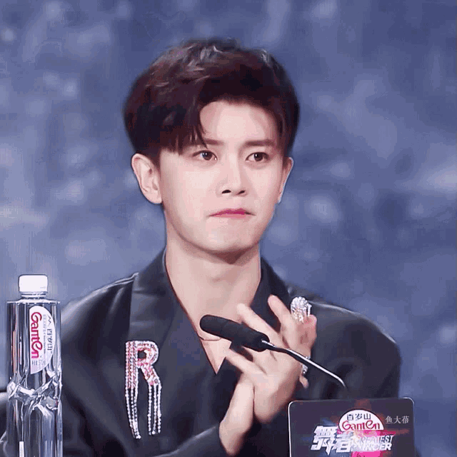 a man sitting in front of a microphone with a bottle of camcal water in front of him