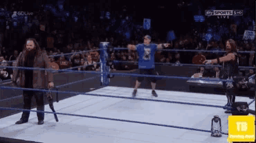 a man in a blue shirt is standing in the middle of a wrestling ring