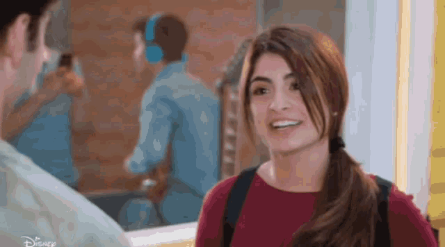a woman in a red shirt is smiling in front of a man wearing headphones ..