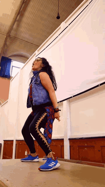 a woman wearing a denim vest and blue adidas shoes