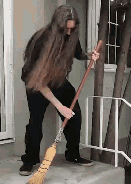 a man with long hair is sweeping the floor with a broom