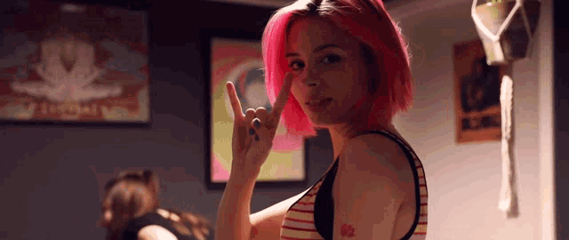 a woman with pink hair and a tattoo on her arm makes a horns sign