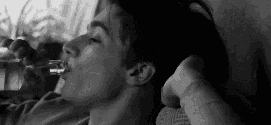 a black and white photo of a man drinking from a glass .